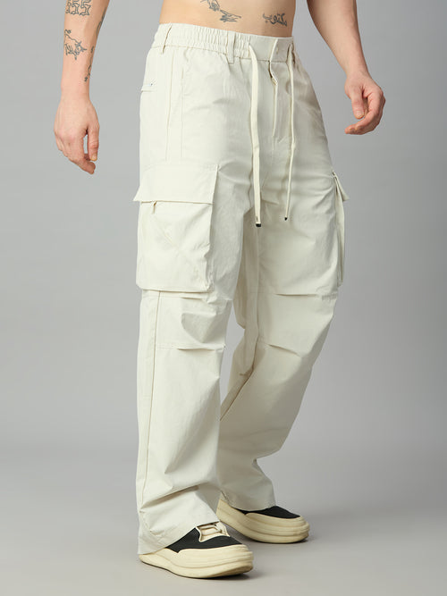 A person modeling a pair of loose, off-white cargo pants with a drawstring waist, shown from the waist down against a plain gray studio background.