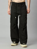 A person wearing black wide-leg cargo pants with a drawstring waist and large side cargo pockets, paired with cream sneakers, photographed against a plain light gray studio background.