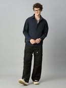 A man wearing a dark navy long-sleeve button-up shirt and black cargo pants, standing against a solid gray studio background.